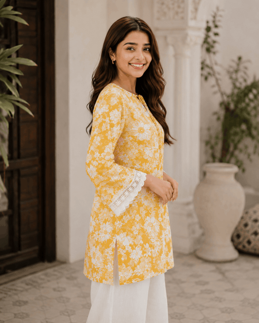 Woman wearing a yellow floral kurta with white pants standing in an outdoor setting.