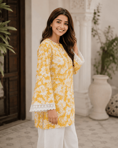 Woman wearing a yellow floral kurta with white pants standing in an outdoor setting.