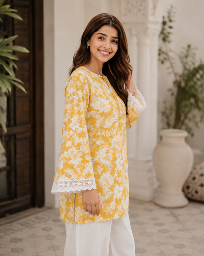 Woman wearing a yellow floral kurta with white pants standing in an outdoor setting.